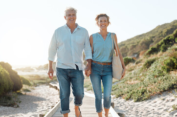 Wall Mural - Senior, couple and walking at the beach with hands in portrait for happiness on a vacation in the outdoor. Mature, woman and man holding by ocean for travel on holiday with sunshine for the weekend.