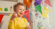 © Kitreel - Close Up Portrait of Little Cute Boy Blowing Bubbles and Laughing at his Birthday Party. Happy Toddler Celebrating and Smiling. Male Kid Using Bubble Bottle in a Living Room Decorated with Balloons.