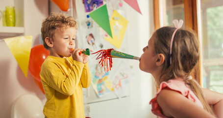 Portrait of Two Little Kids Making Noises with Party Horns on Birthday, Surrounded by Colourful Decorations. Authentic Shot of Old Sister Celebrating her Little Brother's Birthday and Playing with him