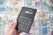 Czarny kalkulator w dloni, kwota wolna od podatku 30 tysiecy pln. W tle gotowka, pieniadze o roznych wartosciach.