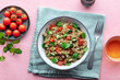 Quinoa tabbouleh salad in a bowl, a healthy dinner with tomatoes and mint, overhead flat lay shot on a pink background