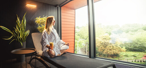 Wall Mural - Woman in white bathrobe lying on sofa and relaxing with orange cocktail at home.