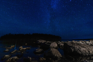 Wall Mural - night landscape with a starry sky over sea water with stones and forest. astrophotography with many 