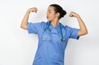 © Roquillo - Young doctor woman wearing blue uniform over isolated background showing arms muscles smiling proud. Fitness concept.