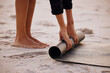 © Kay Abrahams/peopleimages.com - Woman, yoga and beach with hand and feet for rolling mat with clean wellness or fitness. Female person, meditation and yogi on seashore with hands in the outdoor for start in the morning and pilates.
