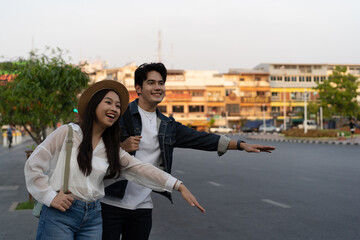 Wall Mural - Happy smiling Young Asian couple traveler tourists hailing for taxi cab on the street in Bangkok in Thailand with no phone or use of technology