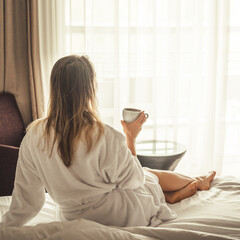 Wall Mural - Woman in white bathrobe lying on sofa and relaxing with cup of tea at home.