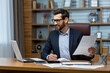 © Liubomir - Mature businessman in shirt doing paperwork, man working with documents, contracts and bills sitting at table using laptop at work, financier accountant with beard and glasses