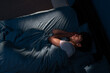 Top view of young man sleeping on cozy bed in his bedroom at night. Blue nightly colors with light shining through the window. People, relax and comfort