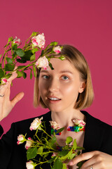 Wall Mural - Portrait of a Beautiful tender young blonde hair girl with the Flowers are growing out of the sleeves of her black blazer. isolated on pink background.