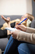 © SlavaStock - Female psychologist writes down main points from client stories in premise. Woman lying on grey sofa tells about sad stories from life