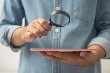 magnifying glass in hand looking at tablet to search internet
