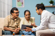 Indian doctor explaining from digital tablet to senior couple about medical report at home - concept of technology, health care support and home consultation.