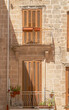 © AngelLuis - Casa al final de la calle Annunziata en el casco antiguo de Polignano a Mare, Italia. Fachada con dos antiguos balcones con contraventanas cerradas en una calle estrecha un día soleado.