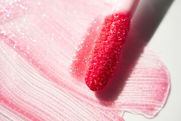 Smears of shining lip gloss and lip gloss brush on white background, hard shadows