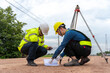 © VStudio - Asian engineer holding tablet to inspect work, with foreman using telescope to check pin against road plan, telescope and radio to control road construction, against road background under construction