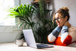© simona - Young entrepreneur taking a break for rest  and touching her neck with a smile watching laptop screen content. Online modern job. People using computer at home on the table surfing the net alone happy
