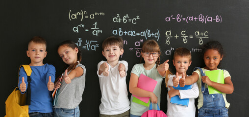 Cute students showing thumb-up near blackboard in classroom