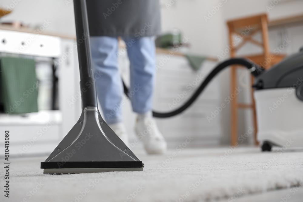 Young woman hoovering carpet in kitchen, closeup