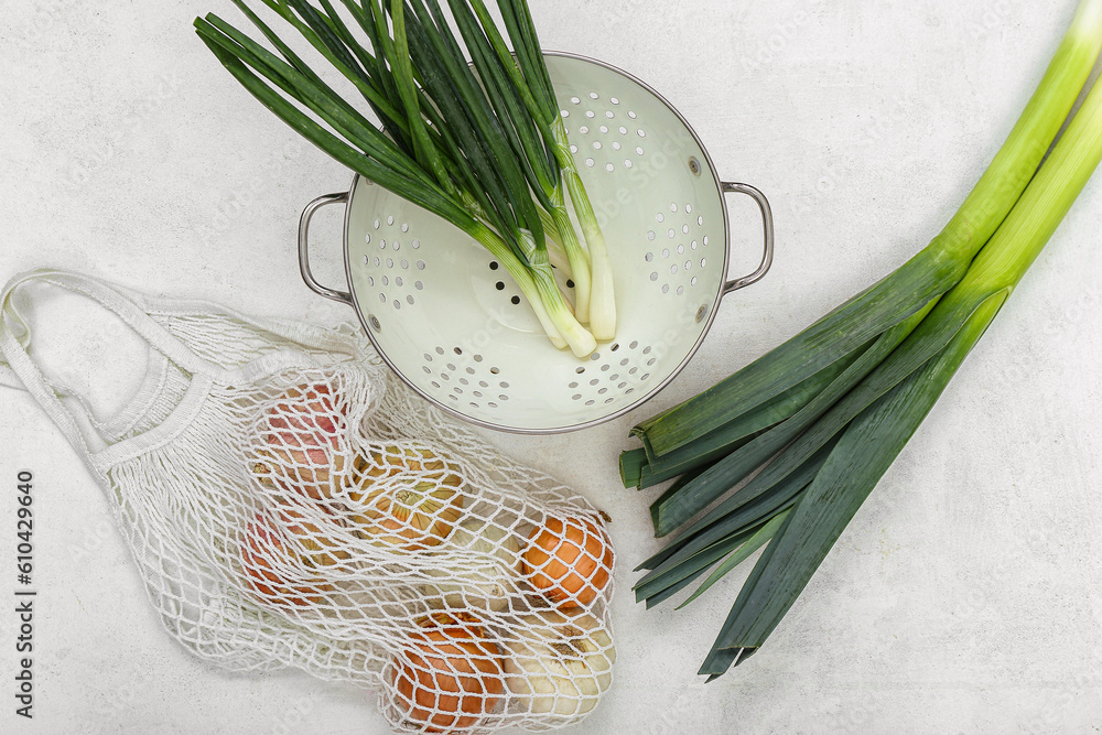 Colander and string bag with different kinds of onion on white background