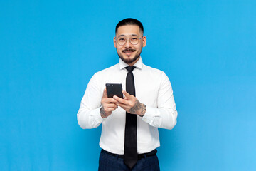 Wall Mural - successful Asian businessman in white shirt and tie uses smartphone on blue isolated background