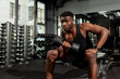 © Богдан Маліцький - athletic african american man trains in dark gym, athletic guy lifts heavy dumbbells in fitness club