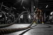 © Богдан Маліцький - athletic african american man trains with ropes in dark gym, motivated guy waving ropes in fitness club