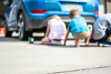 Children sitting on a driveway behind a vehicle in a blind spot out of view of the driver. 