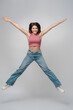 Portrait of excited teenage girl wearing pink top and jeans jumping isolated on gray background