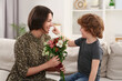 © New Africa - Little son congratulating his mom with Mother`s day at home. Woman holding bouquet of flowers