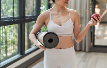 Fitness woman holding yoga mat with Fresh Apple Heathy clean vegan food before working out in yoga studio