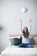 © BestForYou - Joyful woman with a globe on the bed in the living room having fun.