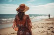 Back view of a young woman in a hat standing on the beach and looking at the sea, A young Bohemian lady wearing boho style clothing on a beach, AI Generated
