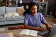 © Seventyfour - Portrait of black young woman working from home and using laptop with dog sleeping in background, copy space