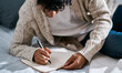 © Felix/peopleimages.com - Notebook, bed and man with home planning, brainstorming and studying notes, education and mental health. Journal, goals and person writing in bedroom for learning, planner and schedule or reminder