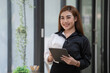 © Songsak C - Smiling young Asian businesswoman holding a digital tablet standing in an office.
