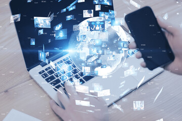 Close up of hands using laptop and cellphone with creative globe with telecommunication picture icons on blurry office workplace background. Business, conference, remote group work. Double exposure.