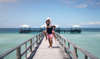 Sticker - Couple, piggyback and outdoor beach deck on a tropical island with love and water on holiday. Summer vacation, travel smile and Maldives playful in nature with freedom and happiness by ocean and sea