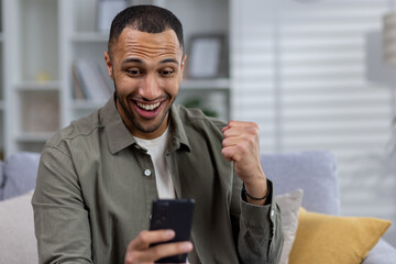 Close-up photo. Young hispanic man rejoices at the received message, reads good news, makes a victory gesture with his hand