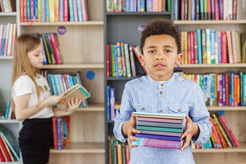 Wall Mural - Afro american child boy choosing books in school library. Benefits of everyday reading.