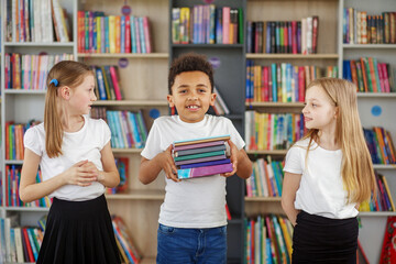 Wall Mural - Children holding stack of books in library. Multiethnic classmates having fun. Back to school.