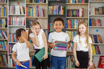 Wall Mural - Four children holding stack of books in library. Multiethnic classmates having fun. Back to school.