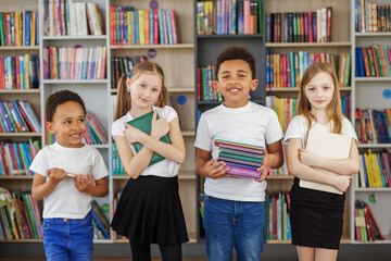 Wall Mural - Four children holding stack of books in library. Multiethnic classmates having fun. Back to school.