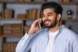 © Ivan - Happy smiling indian professional business man talking on cell phone, eastern businessman making mobile phone call by cellphone in office.