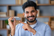 © Ivan - Young arab man with beard wearing casual clothes holding an invisible braces aligner and pointing at it, recommending this new treatment. Dental healthcare concept.