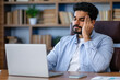 © Ivan - Tired young indian man businessman, worker at work. He has a headache, keeps his hands on his head, sits at a desk in the office