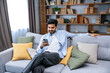 © Ivan - indian millennial bearded man using smart phone for scrolling social media at home