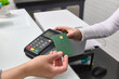 © Taras Grebinets - Selective focus. Customer holding credit bank card with empty space for advertising text, over pos terminal reader, making wireless or cashless payment via NFC technology. Near field technology
