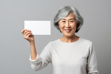 Wall Mural - An Asian middle-aged woman holding up a white card in front of her face. Generative AI.