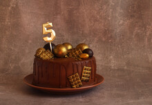 Birthday Chocolate Cake With Gold Balls And A Candle With The Number 5 On A Beige Background